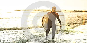 Guy surfer walking with surfboard at sunset in Tenerife - Surf long board training practitioner in action - Sport travel concept
