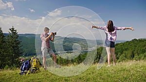 The guy takes pictures of his girlfriend in a picturesque place on the background of the mountains. Nearby are their