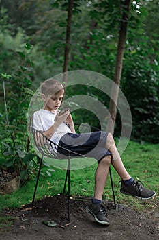 Guy teen sits on chair on nature background and looking at phone. Vertical frame