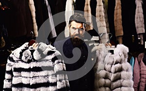 Guy with thoughtful face shows fur coats in fashion store.