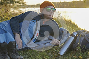 Guy tourist lies in a sleeping bag on the bank of the river.