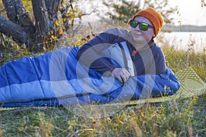 Guy tourist lies in a sleeping bag on the bank of the river.