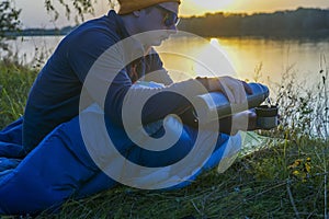 Guy tourist lies in a sleeping bag on the bank of the river.