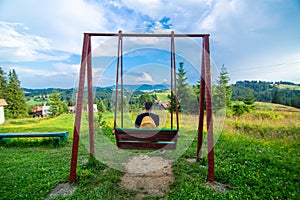 The guy tourist sit on the swing and enjoy amzing nature landscape of summer Karpaty mountains photo