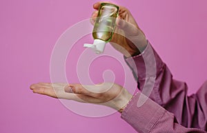 The guy treats his hands with an antibacterial sanitizer. Pink background. Medical content