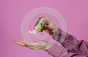 The guy treats his hands with an antibacterial sanitizer. Pink background. Medical content