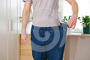 The guy trying on big jeans after losing weight. Man in oversized pants in weight loss concept