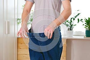 The guy trying on big jeans after losing weight. Man in oversized pants in weight loss concept