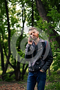 A guy with a twisted orange mustache grimaces on the phone in the park