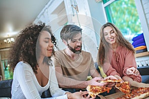 Guy and two girls taking pizza from box.