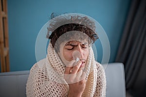 Guy using nose spray. Photo of sick arabic man covered plaid at home. Medical concept