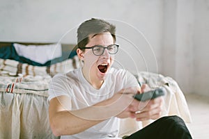 Guy using remote control while sitting on the bed in home. Happy attractive young man watching tv . Human emotions on