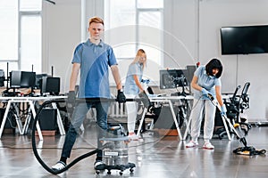 Guy with vacuum cleaner. Group of workers clean modern office together at daytime