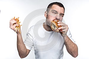 This guy is very delight of junk food. He is biting a big piece of burger and holding a full hand of french fries