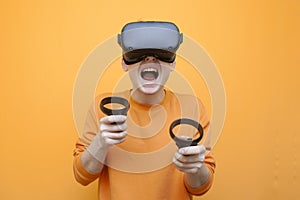 Guy in VR glasses on an orange background, a gamer plays a virtual game and screams