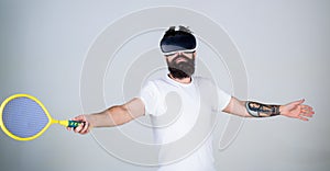 Guy with VR glasses play tennis with racket and ball. Man with beard in VR glasses beating pitch, grey background