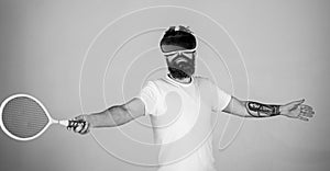 Guy with VR glasses play tennis with racket and ball. Man with beard in VR glasses beating pitch, grey background