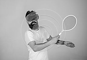 Guy with VR glasses play tennis with racket and ball. Man with beard in VR glasses beating pitch, grey background