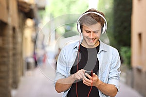 Guy walking and using a smart phone with headphones