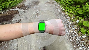 A guy walks on a mountain trail and raises his hand to check something on his smartwatch - chroma key template, first-person view