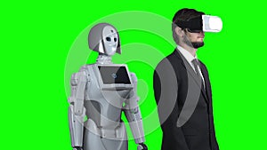 Guy wearing virtual reality glasses and a puts his hand to the side and the robot repeats after him. Green screen. Slow