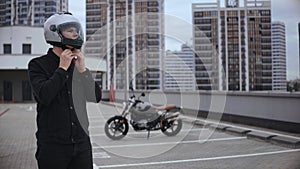 Guy wears motorcycle helmet on top of the parking, in front of motorbike