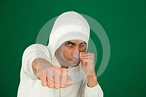 a guy in a white hoodie on a green chromakey background hits the camera with his fist a stern angry look defense attack