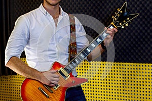 A guy in a white shirt with an electric guitar stands on the recording Studio. The guitarist plays the strings of a musical