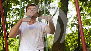 A guy in a white shirt raps in the playground on the street in the summer amid foliage. Medium shot.