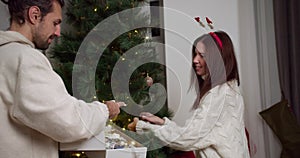 A guy in a white sweatshirt gives his brunette girlfriend in a white sweater New Year's toys and she hangs them on