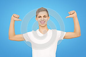 A guy in a white T-shirt with his hands up in the studio on a blue background, isolate