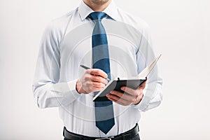 The guy writes in a black notebook. A man on a white background with a blue tie in a white shirt.