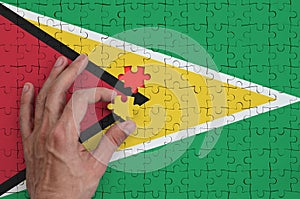 Guyana flag is depicted on a puzzle, which the man`s hand completes to fold