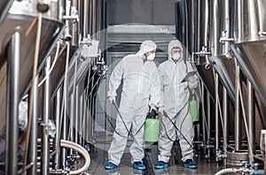 Guys in hazmat suits and masks disinfect brewery kettles at craft plant