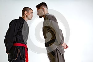 Guys in kimono face to face before karate fight workout on white studio backdrop with copy space, martial arts concept