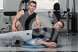 Gym Coach Helping Man On Bosu Abs Exercise