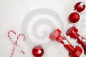 Gym dumbbells and Christmas decorations in white winter snow.