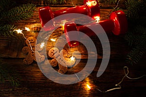 Gym dumbbells and gingerbread man cookies. Christmas flat lay composition with string lights.