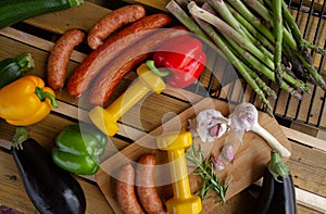 Gym dumbbells, vegetables and sausages for grill. Barbecue party composition, healthy diet choice concept.
