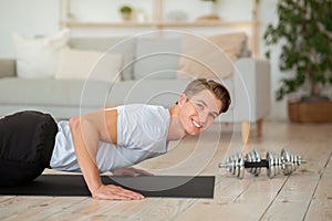 Gym at home. Smiling guy doing push-ups and looking at camera in living room interior