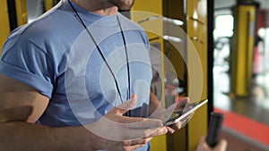 Gym trainer giving explanations to client, gesturing and holding tablet in hands