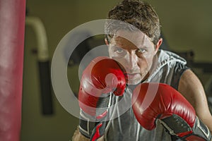 Gym workout portrait of attractive and fierce looking boxer man 30s to 40s in boxing gloves training at fitness club punching