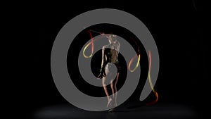 Gymnast gracefully move with a ribbon in his hands. Black background