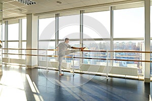 Gymnast in sportswear training near ballet barre in sport gym