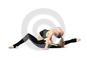 Gymnastic exercises. A flexible little girl in a black tracksuit arches her back and reaches for her leg with her hand