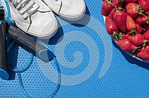 Gymnastic rug, jump rope, sports shoes, plate with strawberries on it. Diet and exercise. Top view. Copy space