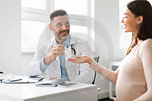 Gynaecology, medicine and pregnancy concept. Male gynecologist giving pills to smiling pregnant woman during appointment