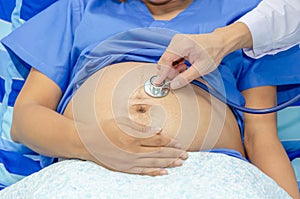 Gynecologist doctor hand checking pregnant young woman with stethoscope on bed in hospital, pregnant woman visit obstetrician doct