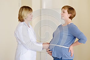 Gynecologist doctor measures with centimeter tape of a pregnant woman. Medical insurance childbearing. Family doctor for gestation