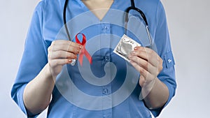 Gynecologist holding red ribbon and condom, AIDS awareness, warning about STI